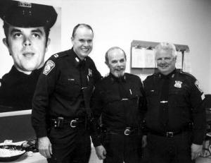 Boston Police Officer Paul Johnston, center, was flanked by Capt. Thomas Lee and Sgt. Herb White at Johnston’s 2003 retirement party at Area C-11 stationhouse. At far left is a photo of a young Paul Johnston as a rookie patrolman. 			Reporter file photo